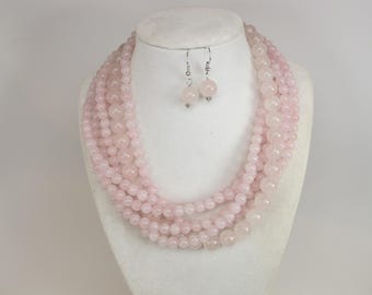May include: A multi-strand necklace and matching earrings made of pink rose quartz beads. The necklace is layered and has a cascading effect.
