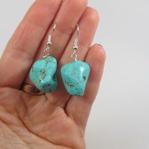 May include: Turquoise dangle earrings with silver hooks. The turquoise stones are a light blue color and have a rough, natural texture.
