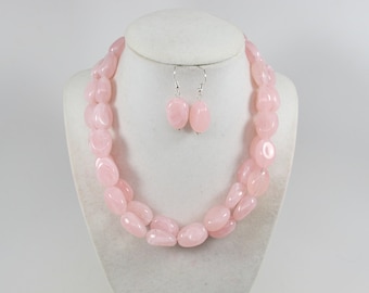 May include: A pink rose quartz necklace and earrings set. The necklace is made of large, smooth, oval-shaped beads. The earrings are simple and dangle.