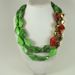 May include: A two-strand necklace with large, irregular beads. The necklace features green, red, and gold-colored beads. The green beads have a marbled effect, while the red beads are translucent. The gold beads have a faceted design.