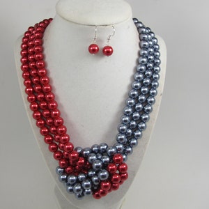 May include: A three-strand pearl necklace with red and gray pearls. The necklace is knotted in the center and has matching red pearl earrings.