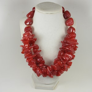 May include: A red chunky statement necklace made of irregular shaped beads. The necklace is layered and has a chunky look.