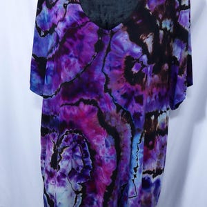 May include: A short-sleeved V-neck shirt with a vibrant tie-dye pattern in shades of purple, blue, and black. The shirt's design features swirling patterns and a soft, flowing fabric, creating a unique and artistic look.