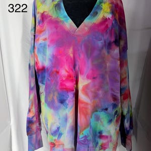 May include: A tie-dye V-neck sweatshirt in a vibrant mix of colors, including pink, purple, blue, and yellow. The long-sleeved top features a relaxed fit and ribbed cuffs. The size is XL, with the number 322 printed on the upper left.