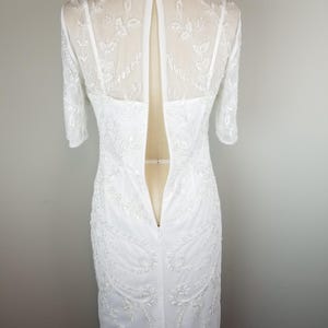 May include: White beaded dress with a sheer back and a zipper closure. The dress has a fitted silhouette and a short sleeve.