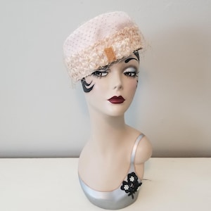 May include: A pink and white pillbox hat with a delicate lace trim and a small bow. The hat is on a mannequin head.