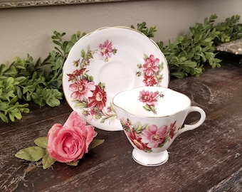Puede incluir: Una taza de té y un platillo blancos con un patrón floral en tonos de rosa y rojo. El diseño floral presenta una variedad de flores, incluyendo rosas y dalias.