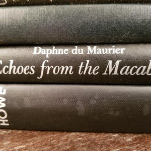 May include: Close-up of three black hardcover books stacked on top of each other. The top book has the title "Echoes from the Macabre" and the author "Daphne du Maurier" printed in white on the spine. The bottom book has the word "HOWE" printed in white on the spine.