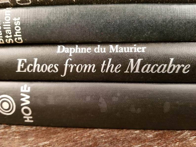 May include: Close-up of three black hardcover books stacked on top of each other. The top book has the title "Echoes from the Macabre" and the author "Daphne du Maurier" printed in white on the spine. The bottom book has the word "HOWE" printed in white on the spine.