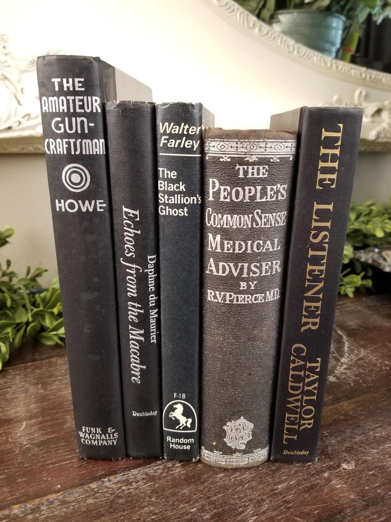 May include: A stack of six black hardcover books with gold lettering. The titles include "The Amateur Gun-Craftsman", "Echoes from the Macabre", "The Black Stallion's Ghost", "The People's Common Sense Medical Adviser", and "The Listener".