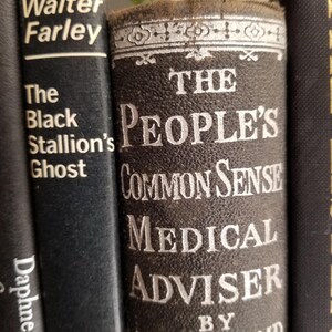 May include: Close-up of three vintage hardcover books with black covers. The middle book has a white title that reads "The People's Common Sense Medical Adviser by R.V. Pierce MD".