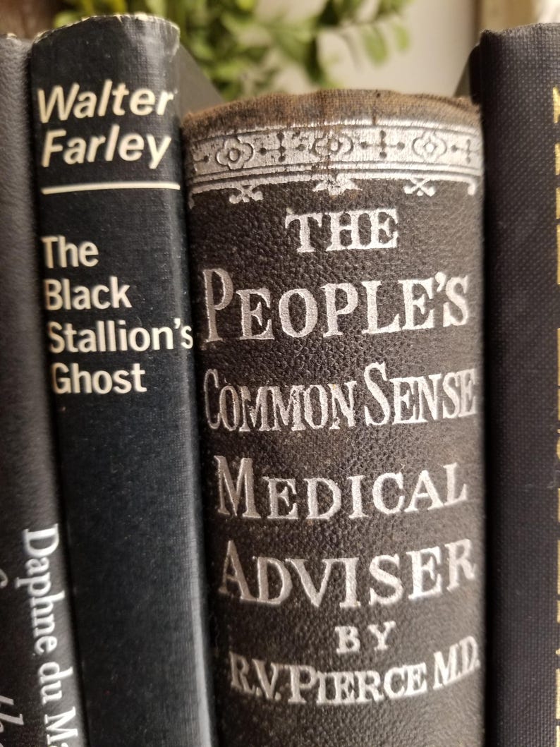 May include: Close-up of three vintage hardcover books with black covers. The middle book has a white title that reads "The People's Common Sense Medical Adviser by R.V. Pierce MD".