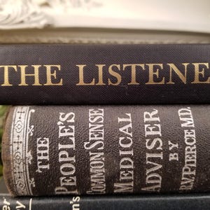 May include: A stack of three vintage hardcover books with black covers. The top book has gold lettering that reads "THE LISTENER". The second book has white lettering that reads "THE PEOPLE'S COMMON SENSE MEDICAL ADVISER BY R.V. PIERCE MD."