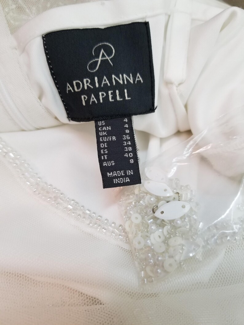 May include: White dress tag with black text that reads "Adrianna Papell" and size information in US, Canadian, UK, EU/FR, German, Spanish, Italian, and Australian sizes. The tag also reads "Made in India".