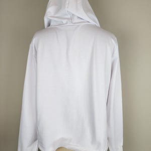 Puede incluir: Una sudadera con capucha blanca de manga larga, con una capucha sin cordones, mangas largas con pu&ntilde;os acanalados y un dobladillo recto. La prenda est&aacute; confeccionada con un tejido liso y sencillo, y se muestra desde la vista posterior.