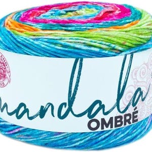 May include: A cylindrical skein of Lion Brand Mandala Ombré yarn featuring a vibrant gradient of colors including hot pink, orange, yellow, lime green, and various shades of blue. The white paper label displays the text mandala OMBRE.