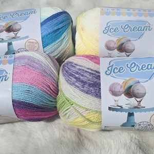 May include: Four skeins of Lion Brand Ice Cream yarn in various pastel colors. Each skein has a label with the words "Ice Cream" and an illustration of ice cream sundaes. The yarn colors include blue, yellow, pink, purple, and green.