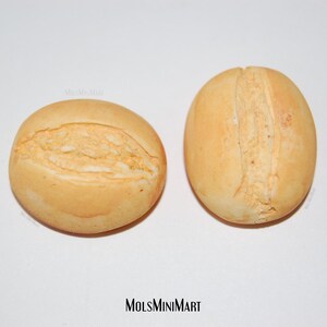 May include: Two small, round, light brown bread rolls with a single seam down the center.