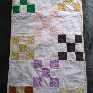May include: A white quilt with a patchwork design. The quilt is made up of nine squares, each with a different pattern. The patterns include a green and white checkerboard, a pink and white checkerboard, a yellow and white checkerboard, a brown and white checkerboard, a purple and white checkerboard, a yellow and white floral pattern, a brown and white floral pattern, and a white and yellow floral pattern.
