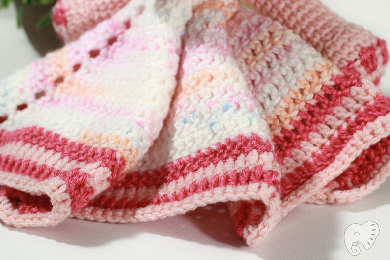 May include: A crocheted baby blanket with pink, white, and peach stripes. The blanket has a delicate, lacy pattern and a pink border.