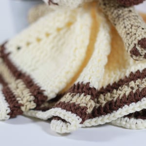 May include: A crocheted baby blanket with a brown and cream striped border. The blanket is made with soft yarn and has a cute animal head attached.