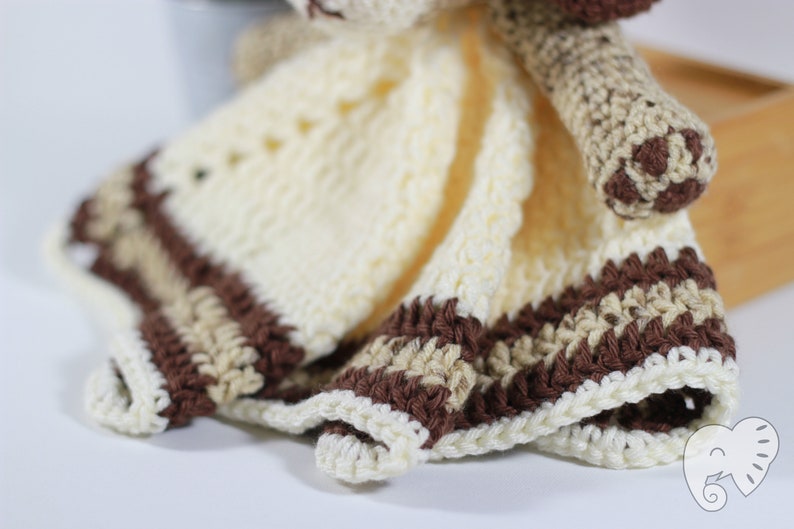 May include: A crocheted baby blanket with a brown and cream striped border. The blanket is made with soft yarn and has a cute animal head attached.