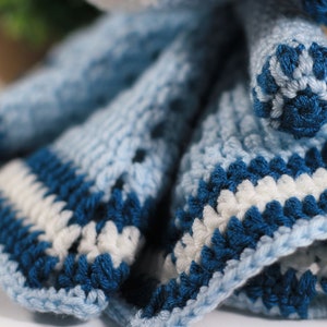 May include: A crocheted doll dress with blue and white stripes. The dress is made with a textured yarn and has a ruffled hem.