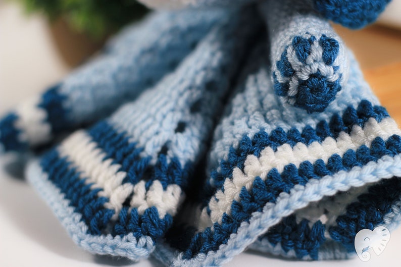 May include: A crocheted doll dress with blue and white stripes. The dress is made with a textured yarn and has a ruffled hem.