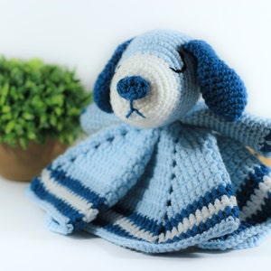 May include: A blue and white crocheted baby blanket with a blue crocheted dog attached. The dog has white fur and blue ears.