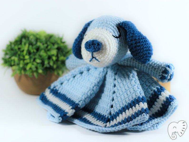 May include: A blue and white crocheted baby blanket with a blue crocheted dog attached. The dog has white fur and blue ears.