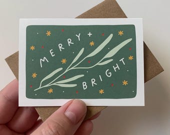 May include: A green Christmas card with a white sprig of leaves and the text "Merry + Bright" in white with red stars.