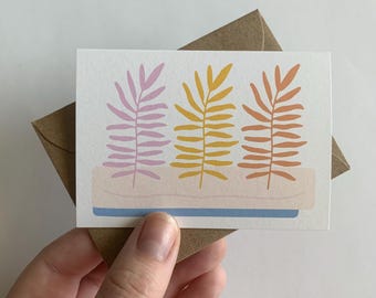 May include: A greeting card with a simple design featuring three stylized plants in a pot. The plants are pink, yellow, and orange.