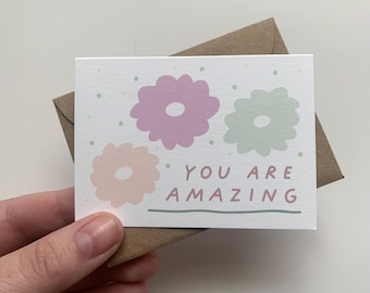 May include: A white card with three pastel colored flowers and the text "You are amazing" in pink and green.