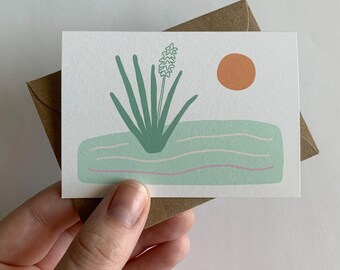 May include: A greeting card with a green plant with a white flower on a light blue background with a pink and white wavy line and an orange sun.