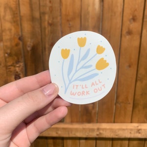 May include: White circle sticker with a blue and yellow floral design and the text "It'll all work out".