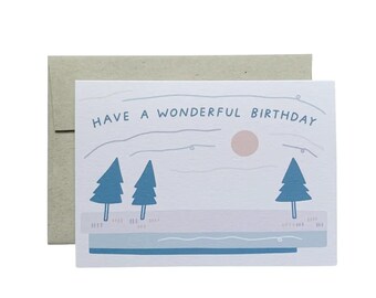 May include: A white card with a blue and pink illustration of a winter scene with two pine trees and a sun. The text "HAVE A WONDERFUL BIRTHDAY" is written in blue.