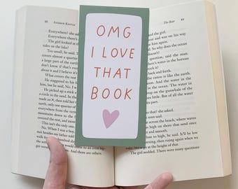 May include: A green bookmark with a pink heart and the text "OMG I LOVE THAT BOOK" in white and red letters. The bookmark is placed in a book with text about the ocean.