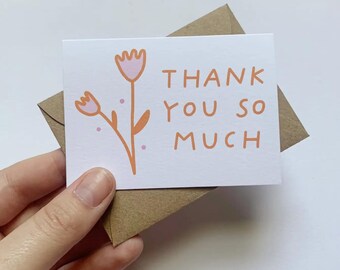 May include: A white card with a pink and orange flower illustration and the text "THANK YOU SO MUCH". The card is in a brown envelope.