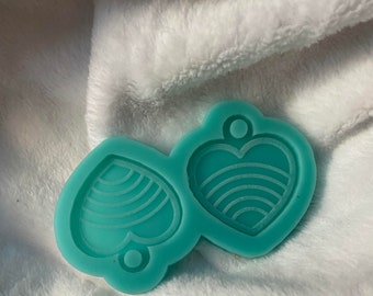 May include: A teal silicone mold with two heart-shaped cavities. One heart has a striped pattern and the other has a wavy pattern.