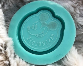 May include: A teal blue silicone mold with a raised design of Mickey Mouse's head. The mold has a circular shape and the text "PASSHOLDER" is inscribed around the edge of the design.