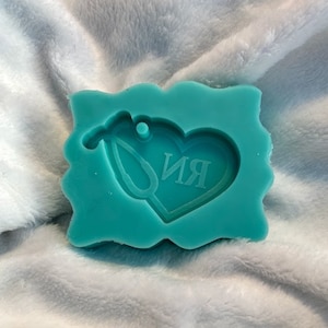 Puede incluir: Molde de silicona azul turquesa con forma de corazón y diseño de estetoscopio. El corazón tiene las letras "RN" en su interior.