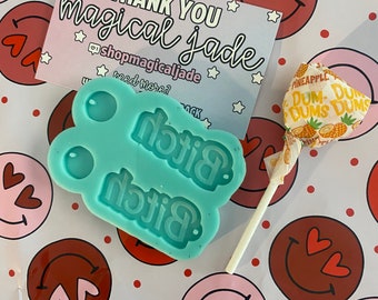 Può includere: Uno stampo in silicone blu turchese con la parola "Bitch" in rilievo due volte. Lo stampo è su uno sfondo bianco con un motivo di faccine sorridenti rosa e rosse. Nell'immagine è presente anche un lecca-lecca con un design a forma di ananas.