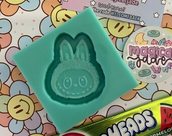 May include: A teal silicone mold featuring a cartoon bunny face, alongside a "Thank You" card from "magical jade" and a watermelon Airheads candy. The background is a floral pattern with smiley faces.
