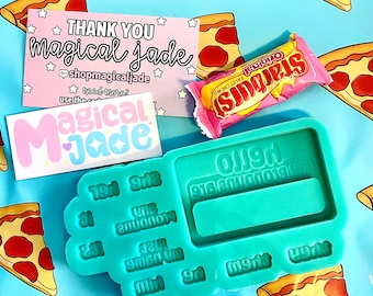 May include: A teal blue silicone mold shaped like a vintage calculator with the numbers 19, 912, 21, 23, 916, 201, 9r1, 9r2, and 9r3 printed on the mold. The mold is on a blue background with pizza slices printed on it. A pink Starburst candy bar and a pink business card with the text "THANK YOU magical jade" are also in the image.