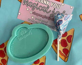 May include: A light blue silicone mold shaped like a cloud with the word "Disneyland" written on it. The mold is on a blue background with a pizza slice pattern. There is a thank you card with the text "THANK YOU magical jade shopmagicaljade need more? use the code WELCOMEBACK" and a lollipop with blue and white wrappers.