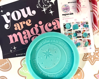 May include: A teal blue silicone mold with a crescent moon and star design. The mold is on a white background with gingerbread cookie-shaped stickers. The text on the mold reads "And the dreams are first signs to the stars who listen".
