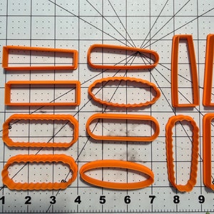 Puede incluir: Conjunto de diez cortadores de galletas de plástico naranja en varias formas, incluyendo rectángulos, óvalos y bordes ondulados. Los cortadores están dispuestos sobre una superficie blanca cuadriculada.