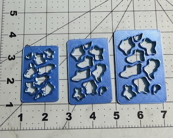 May include: Three blue plastic stencils with a cow print design. The stencils are different sizes and are arranged from smallest to largest.
