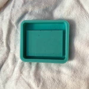 May include: A teal silicone mold for resin casting. The mold has a rectangular shape with a raised inner rectangle for creating a tray.