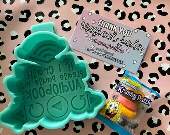 May include: A teal plastic cookie cutter with an embossed design featuring a play button, a refresh icon, and text that reads "If I crash please pause and reboot". Beside it is a small package of Krabby Patties candy and a thank you card.